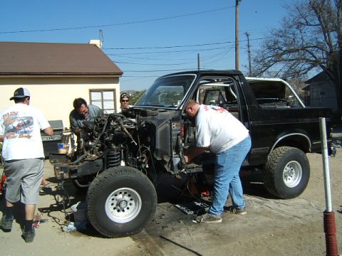 1988 Ford Bronco - Three men are gathered around the front of a black Ford Bronco, appearing to work on its engine and front-end components.
