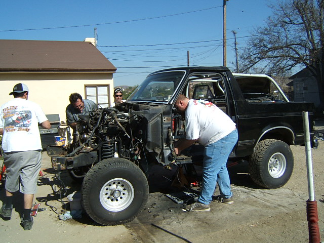 Men working on the engine of a black Ford Bronco. The front end is disassembled