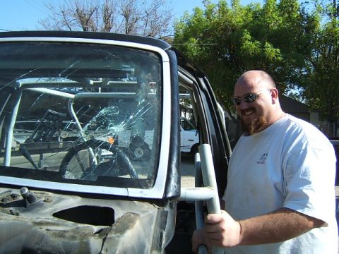 1988 Ford Bronco - A man stands beside a heavily damaged black SUV, its windshield shattered and interior reinforced with a roll cage.