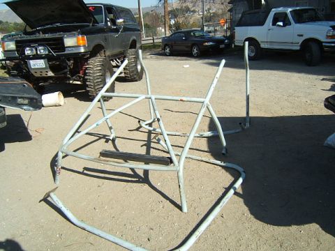 1988 Ford Bronco - A roll cage lies on the ground in front of a lifted black Ford Bronco and a white Ford Bronco.