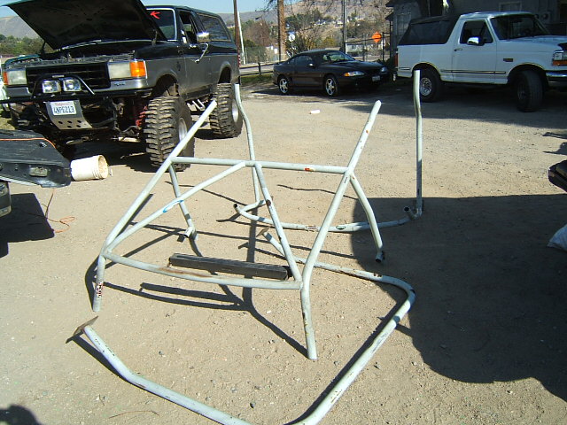 Roll cage on dirt with lifted Bronco and white Bronco in background