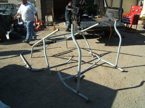 1988 Ford Bronco - Roll cage tubing is spread out on the dirt next to a pickup truck.