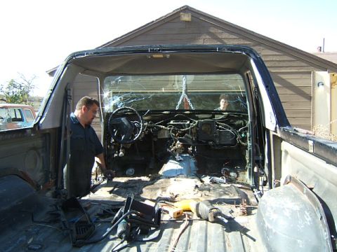 1988 Ford Bronco - A man works on the interior of a vehicle that has been stripped down to its bare components.