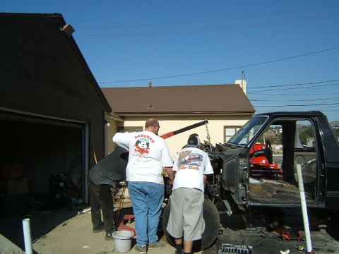 1988 Ford Bronco - Three men work on a black 1988 Ford Bronco, with its engine removed and a hoist assisting.
