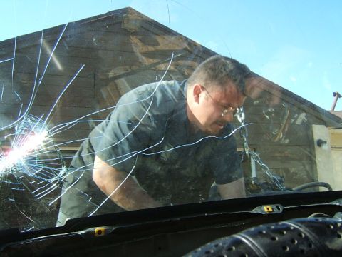 1988 Ford Bronco - A man is seen working inside a vehicle, viewed through a heavily cracked windshield.