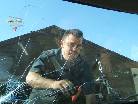 1988 Ford Bronco - A man works on an engine, viewed through a heavily cracked windshield with several stickers adhered to the glass.