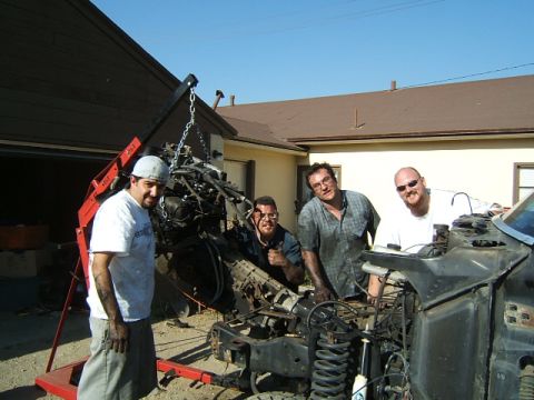 1988 Ford Bronco - Men work on removing an engine from a vehicle chassis using an engine hoist.