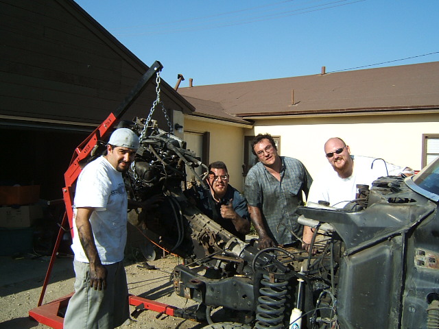 Four men with an engine hoist removing an engine from a vehicle chassis