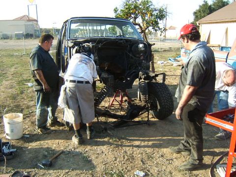 1988 Ford Bronco - Several men are gathered around a disassembled truck chassis, appearing to be in the process of repair or restoration.