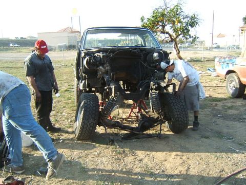 1988 Ford Bronco - The front end of a disassembled 1980s Ford Bronco is visible, with two men attending to the chassis.