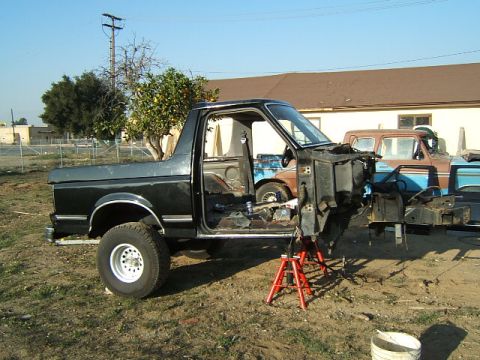 1988 Ford Bronco - A disassembled Ford Bronco sits on jack stands outdoors, with another vehicle visible in the background.