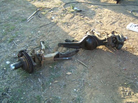 1988 Ford Bronco - Two disassembled axle assemblies lie on the dirt ground, likely for a Ford Bronco.