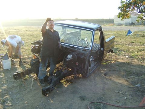 1988 Ford Bronco - Two men work on a disassembled truck chassis in a field at sunset.
