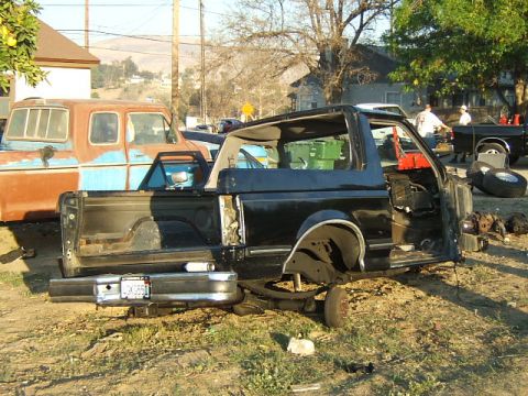1988 Ford Bronco - A black SUV is partially disassembled in a yard with other vehicles present.