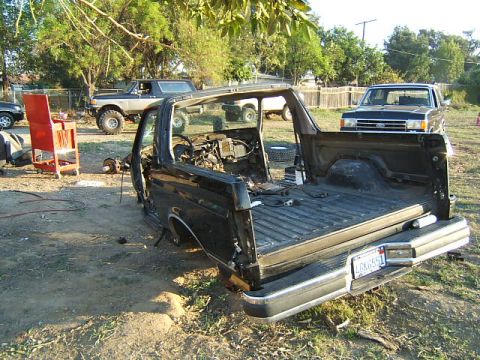 1988 Ford Bronco - This black Ford Bronco is missing its doors and roof, with parts scattered around it.