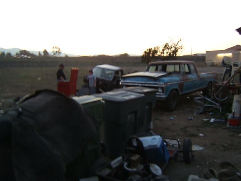 1988 Ford Bronco - Yard scene with a blue pickup and a dark SUV, possibly awaiting repair or parts.