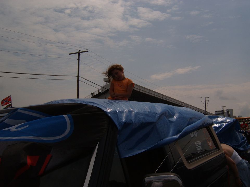 kid sitting on blue tarp covering vehicle, Ford logo visible on tarp