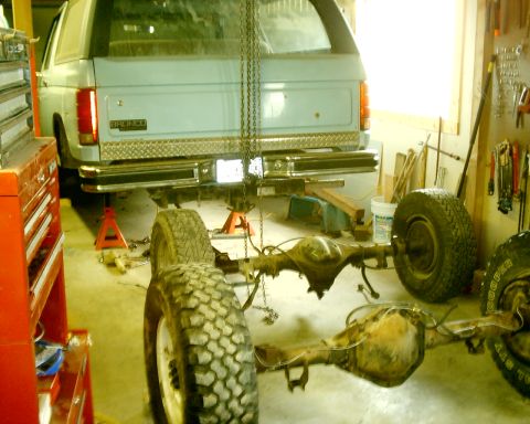 1985 Ford Bronco - The rear axle of a 1985 Ford Bronco is detached and on the floor, while the vehicle is supported by jack stands.