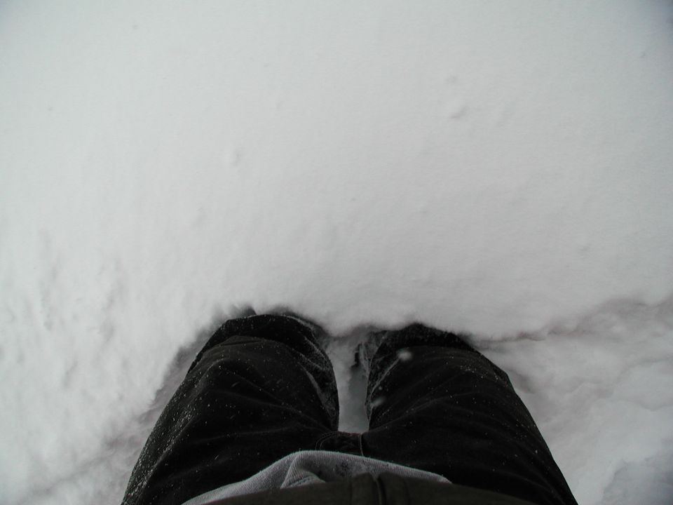 Looking down at black pants and shoes standing in deep fresh snow