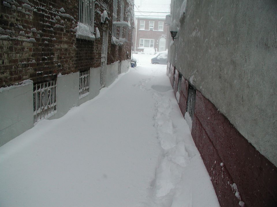Snow-filled narrow alley between brick and stucco buildings, single footpath