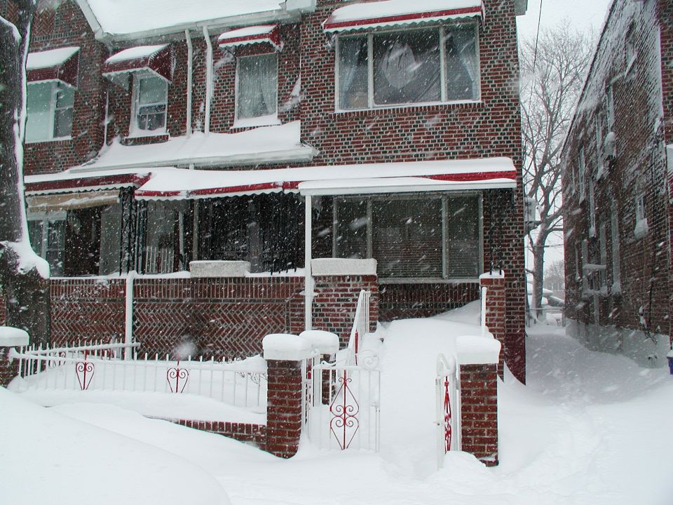 Brick rowhouse with red awnings buried in heavy snowfall behind a white fence