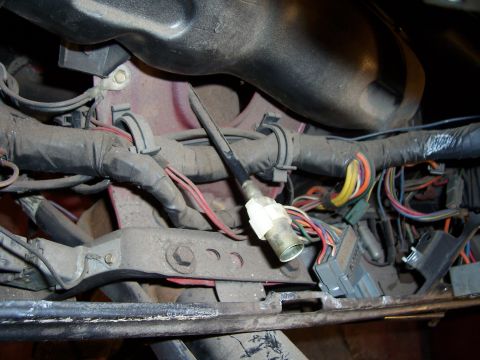 1978 Ford Bronco - Dusty under-dash view showing the speedometer cable with its knurled threaded end and white plastic quick-disconnect fitting routed among t…
