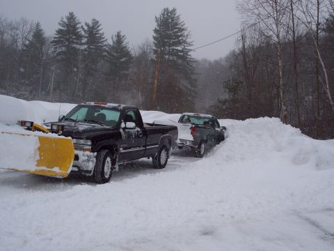 2001 Ford Crown Victoria - A black pickup truck equipped with a snow plow is seen in a snowy scene, with another truck partially obscured by snow in the background.