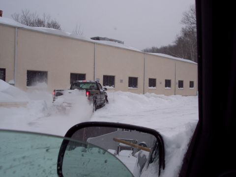2001 Ford Crown Victoria - A pickup truck kicks up snow as it drives past a building during a snowstorm.