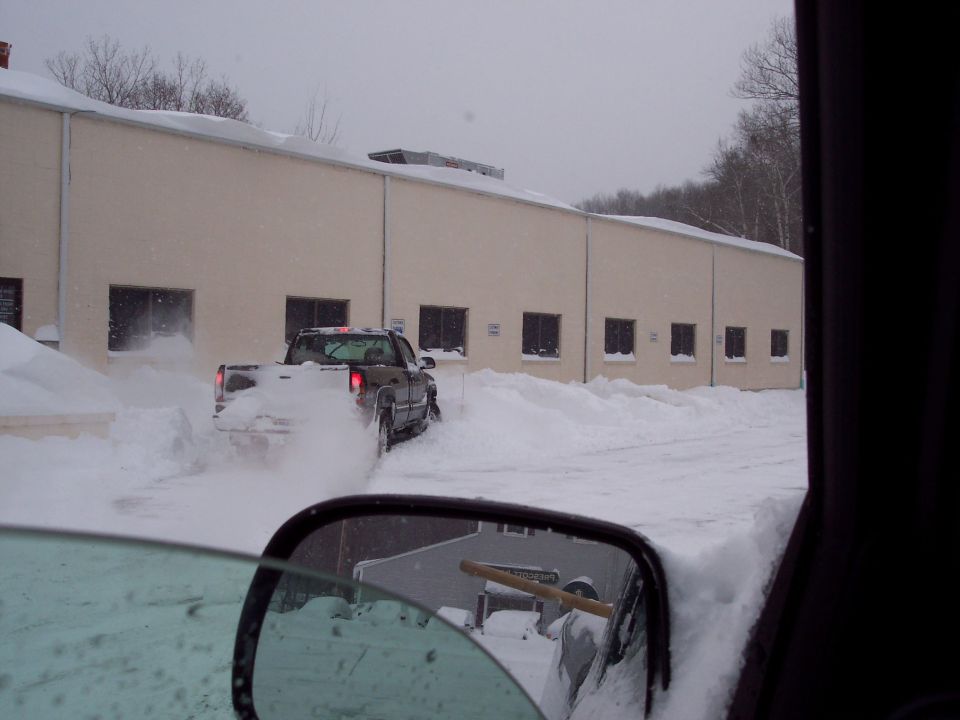 Pickup truck driving through deep snow near a building