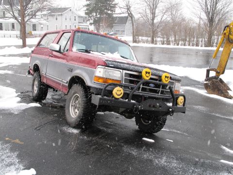 1995 Ford Bronco - A red and silver Ford Bronco sits in a snowy lot next to a yellow excavator.