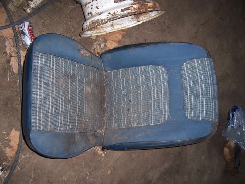 1983 Ford Bronco - A worn blue and striped vehicle seat sits on the ground next to a rusty wheel rim and a discarded soda can.