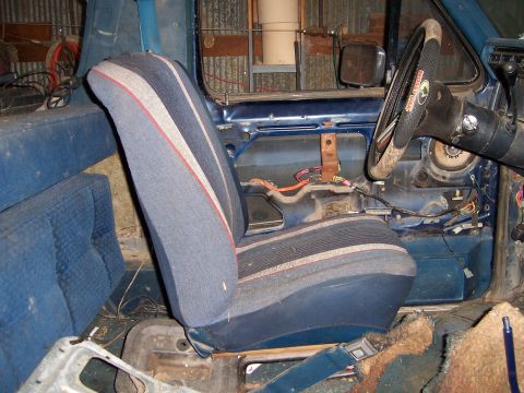 1983 Ford Bronco - The interior of a blue vehicle shows exposed wiring and striped seats.