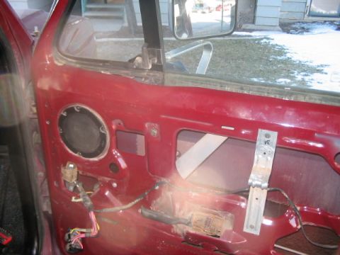 1991 Ford Bronco - The interior of a red car door shows exposed wiring and the window mechanism, with a speaker mounted in the panel.