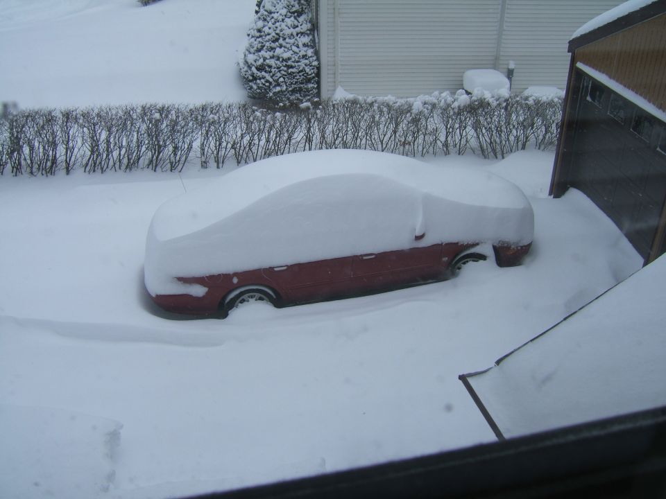 Red sedan covered in snow, seen from the side in a driveway
