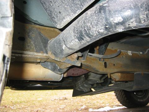 1996 Ford Bronco - Undercarriage view along the frame rail of a lifted truck, showing surface rust on the boxed frame, a body mount and bracket, brake and fue…