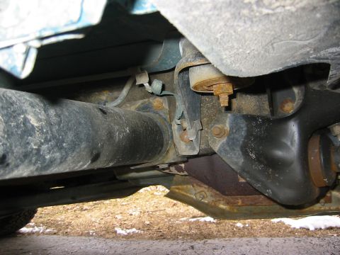 1996 Ford Bronco - Close-up under a truck showing a rubber body mount bushing with its rusty through-bolt and washer sandwiched between the frame rail and flo…