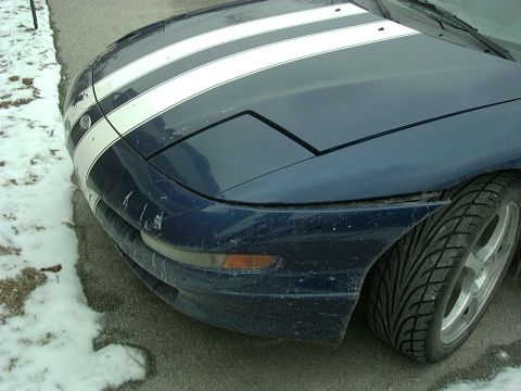 1995 Ford Probe - A blue 1995 Ford Probe with white racing stripes is seen from the front, showing its pop-up headlights and a snowy roadside.