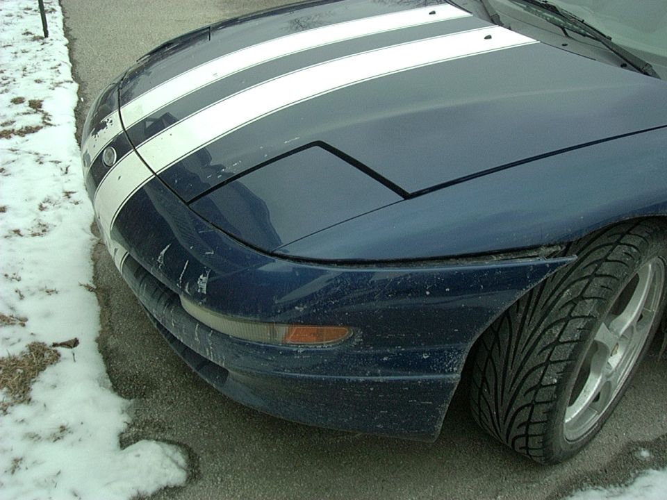 Front view of a blue 1995 Ford Probe with white racing stripes and pop-up headlights