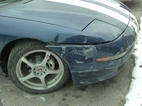1995 Ford Probe - The front fender and bumper of a blue car with white racing stripes show significant damage and scuff marks.