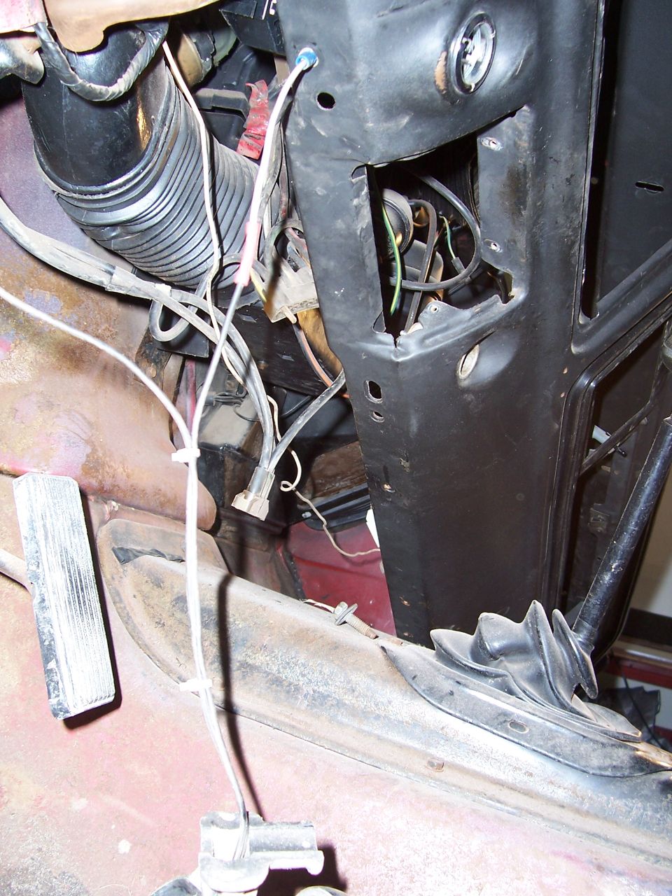 Close-up of vehicle interior showing wiring, a black flexible duct, and part of a pedal assembly