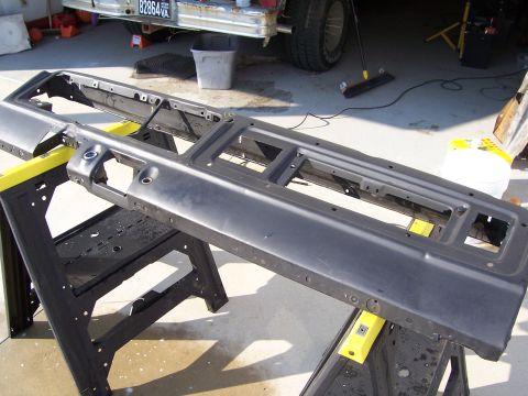 1978 Ford Bronco - Two stripped dashboard/instrument-panel structures laid across yellow-topped sawhorses on a driveway, cleaned down to bare gray metal with…