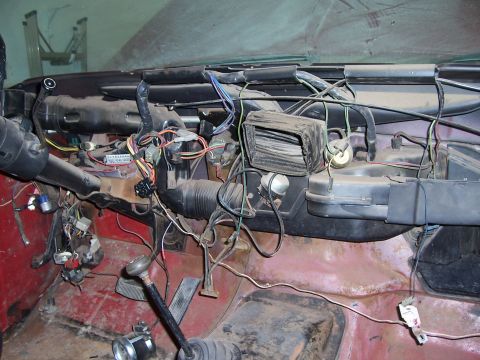 1978 Ford Bronco - Wide interior shot behind a removed dash pad, exposing the full instrument-panel wiring harness with color-coded connectors, the steering c…