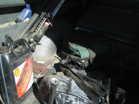 1990 Ford Bronco - Hi-Lift style jack and a Shell oil jug are stored on the floor behind a folded rear seat inside a vehicle.
