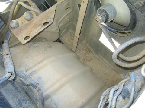 1990 Ford Bronco - dusty empty corner of an engine bay showing mounting brackets, braided lines and bare painted sheet metal.