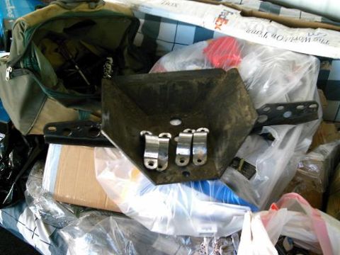 1986 Ford Bronco - Unidentified black metal automotive part with silver clamps, amidst clutter.