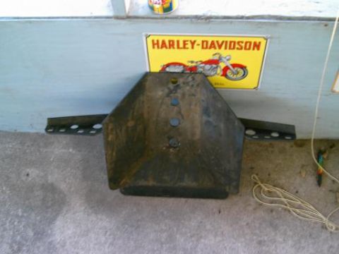 1986 Ford Bronco - A metal part with mounting brackets is displayed in front of a Harley-Davidson sign.