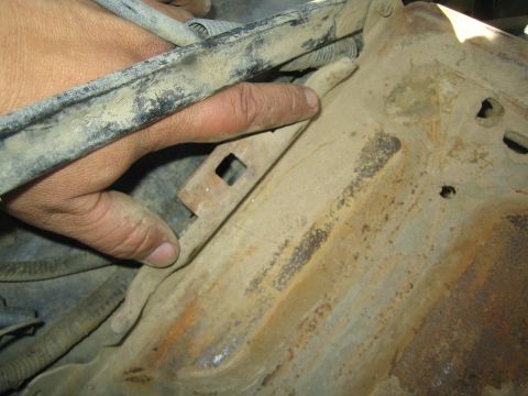1990 Ford Bronco - hand grips a worn dusty bar next to a heavily rusted, dirt-caked stamped metal panel in an engine bay.