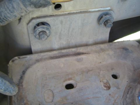 1990 Ford Bronco - Two bolts secure a bracket above a dusty, rust-streaked stamped metal plate with mounting holes underneath.