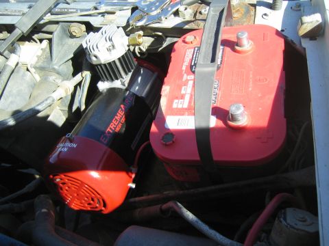 1990 Ford Bronco - red Optima battery is strapped in beside a red and silver ExtremeAire High Output compressor in an engine bay.