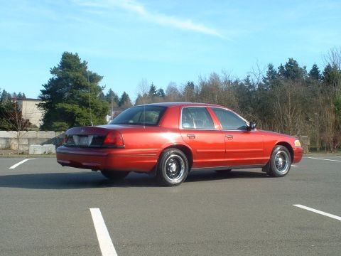 1999 Ford Crown Victoria - The rear of a red sedan is visible in this outdoor parking lot scene.